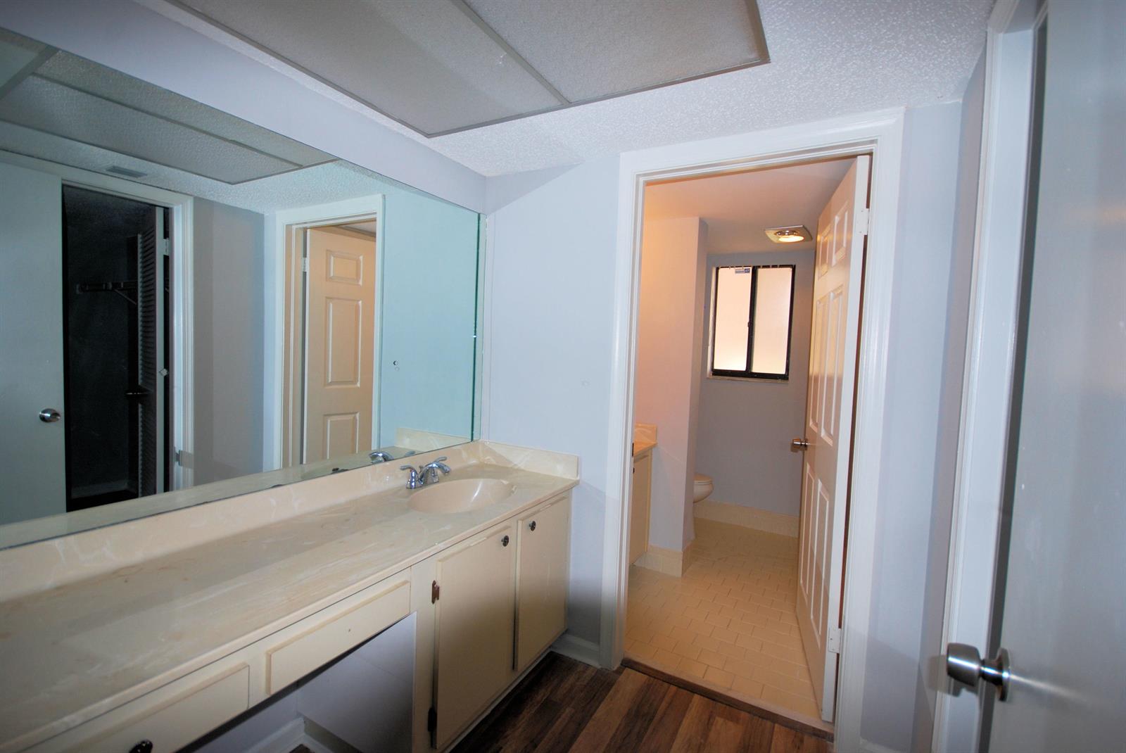 A bathroom vanity with a large mirror leads into a separate room with a toilet — 5917 Via Vermilya # 308, Lake Worth FL 33462, LAKE WORTH, FL