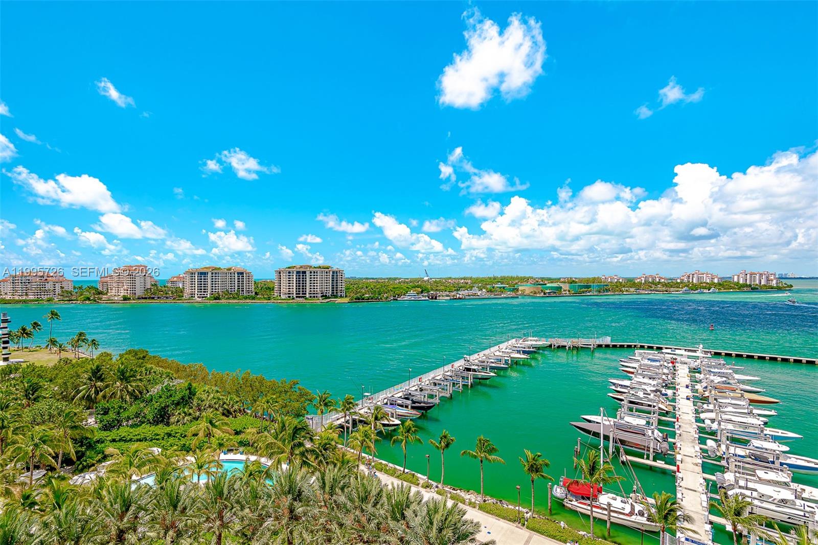 An elevated view of a marina with docked boats, palm trees, and distant waterfront buildings — 1000 S Pointe Drive # 905, Miami Beach FL 33139, MIAMI BEACH, FL