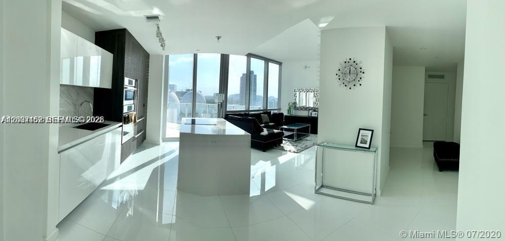 A modern open-concept kitchen and living area features white glossy cabinets, tile floors, and floor-to-ceiling windows — MIAMI, FL