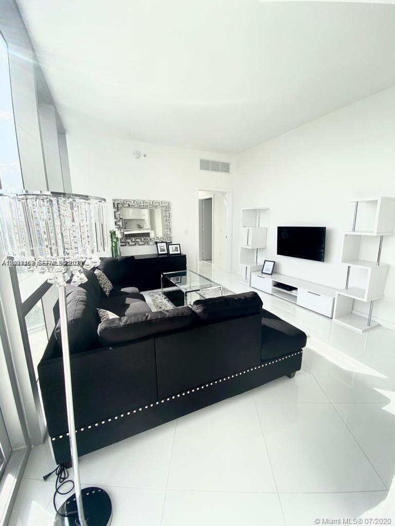 A modern living room features a black sectional sofa, a glass coffee table, and white shelving — MIAMI, FL