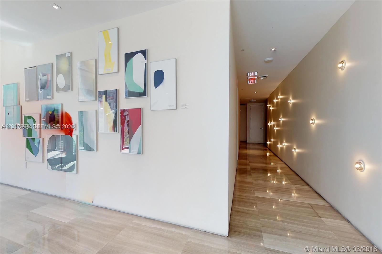 A hallway with a gallery wall of framed art and wall-mounted light fixtures — 460 NE 28th ST # 1102, Miami FL 33132, MIAMI, FL