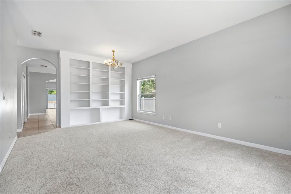A carpeted living room features a built-in white bookshelf and a chandelier — 7933 REX HILL TRAIL, ORLANDO, FL