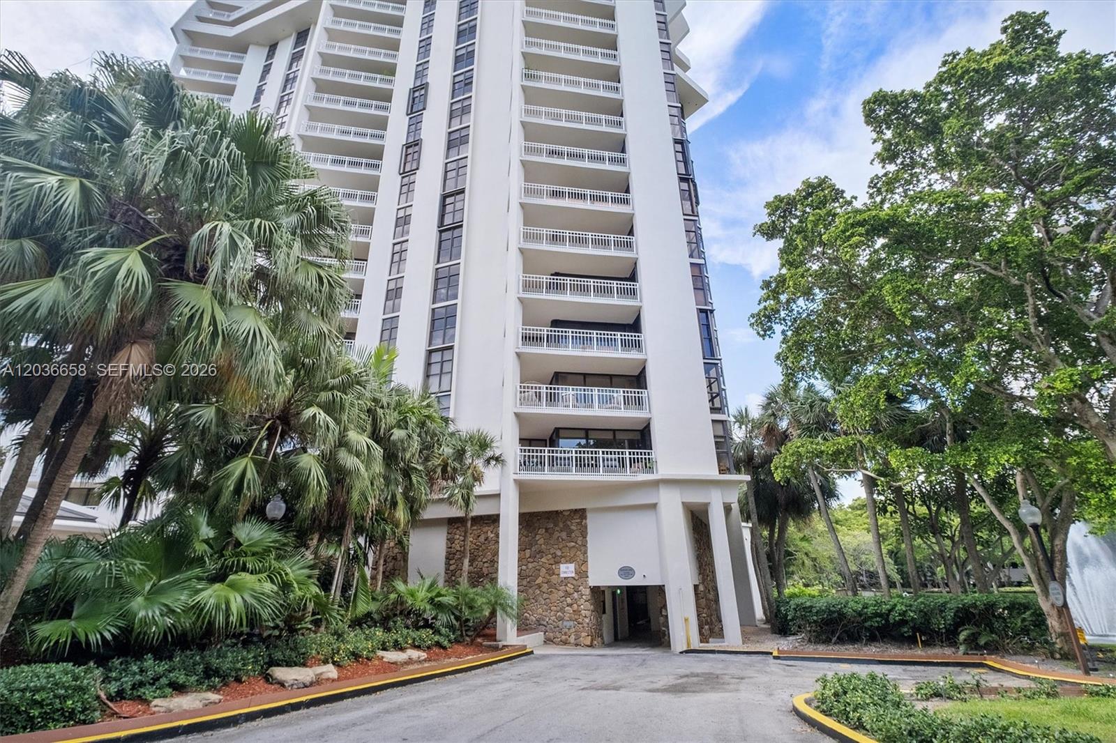 A tall white residential high-rise building features stacked balconies and a stone-clad ground level entrance — 1000 Quayside Ter # 411, Miami FL 33138, MIAMI, FL