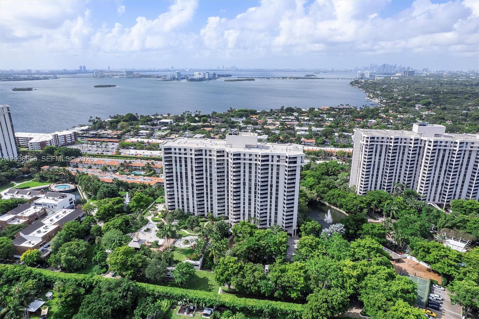 An aerial view shows two large residential buildings surrounded by lush trees and a lake — 1000 Quayside Ter # 411, Miami FL 33138, MIAMI, FL