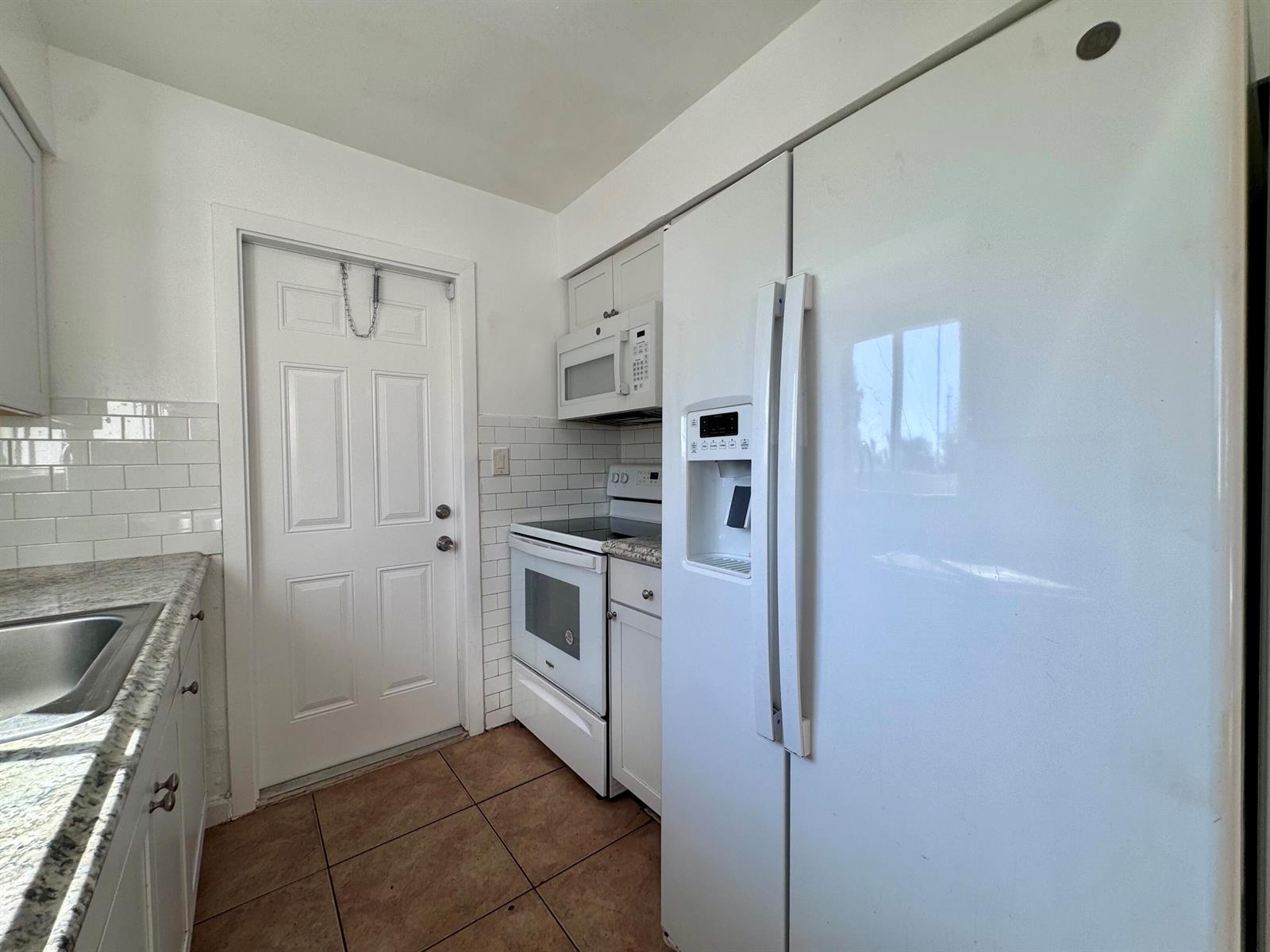 A kitchen features white cabinets, granite countertops, a stainless steel sink, and white subway tile — 3101 NE 7th Avenue # B, Pompano Beach FL 33064, POMPANO BEACH, FL