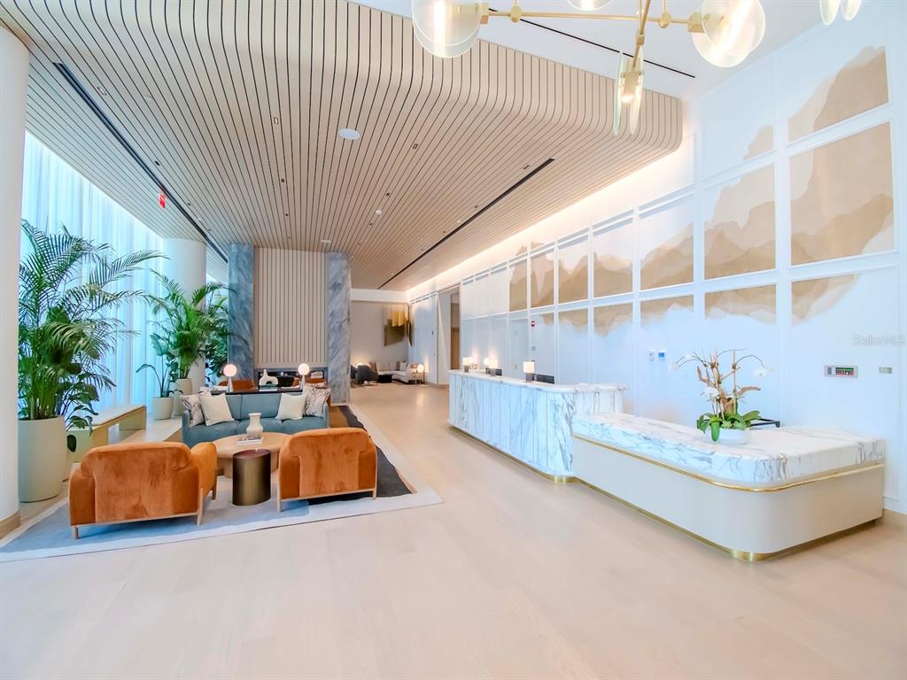A modern lobby features a marble reception desk, orange armchairs, and a slatted wood ceiling — 3101 W BAYSHORE BOULEVARD UNIT 2304, TAMPA, FL