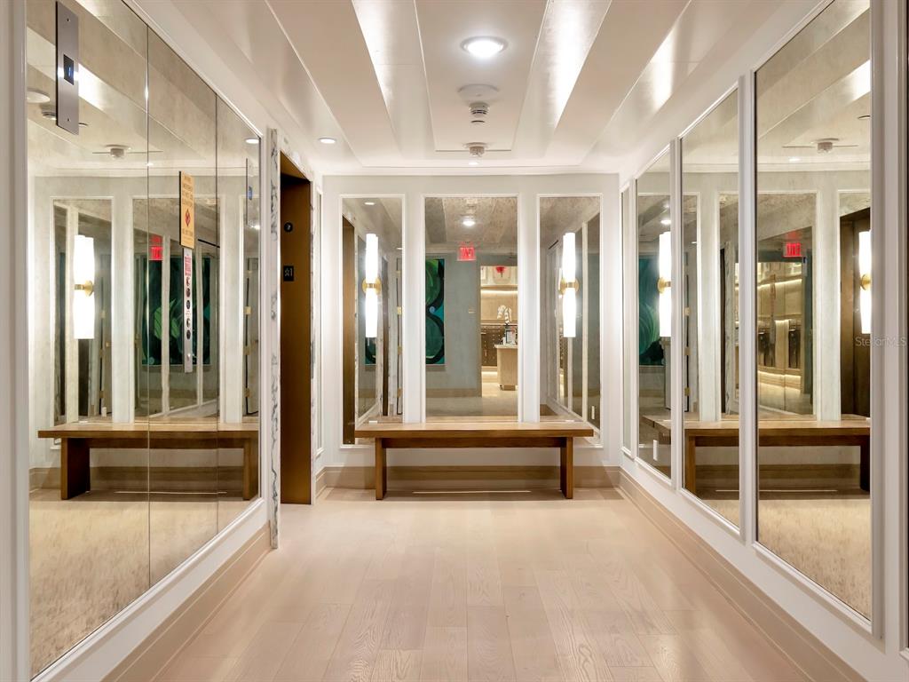A hallway with light wood floors, mirrored walls, and wooden benches on both sides — 3101 W BAYSHORE BOULEVARD UNIT 2304, TAMPA, FL