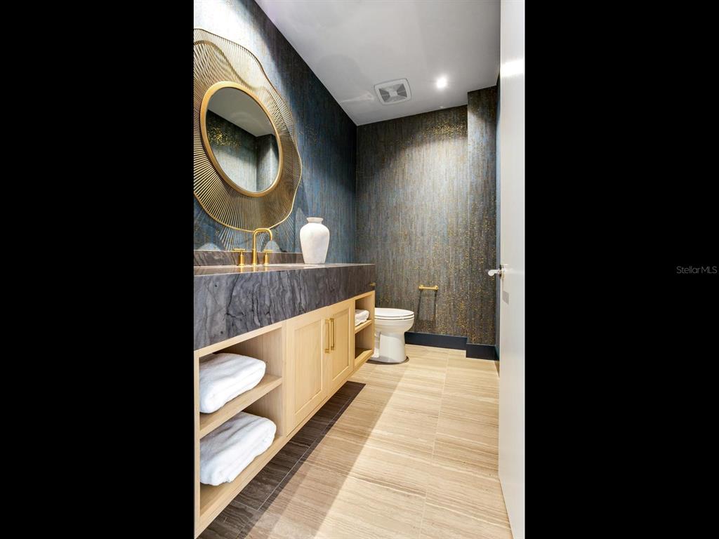 A modern powder room features a stone vanity, gold-framed mirror, and textured blue wallpaper — 3101 W BAYSHORE BOULEVARD UNIT 402, TAMPA, FL