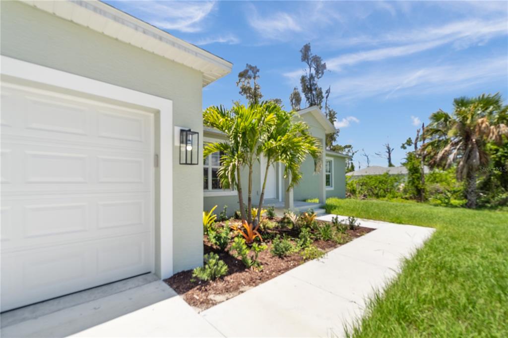 A light green house exterior features a white garage door, a palm tree, and landscaping — 12107 BROOKSIDE AVENUE, PORT CHARLOTTE, FL
