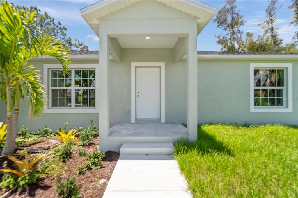 A light green house exterior features a covered entryway with a white door and windows — 12107 BROOKSIDE AVENUE, PORT CHARLOTTE, FL