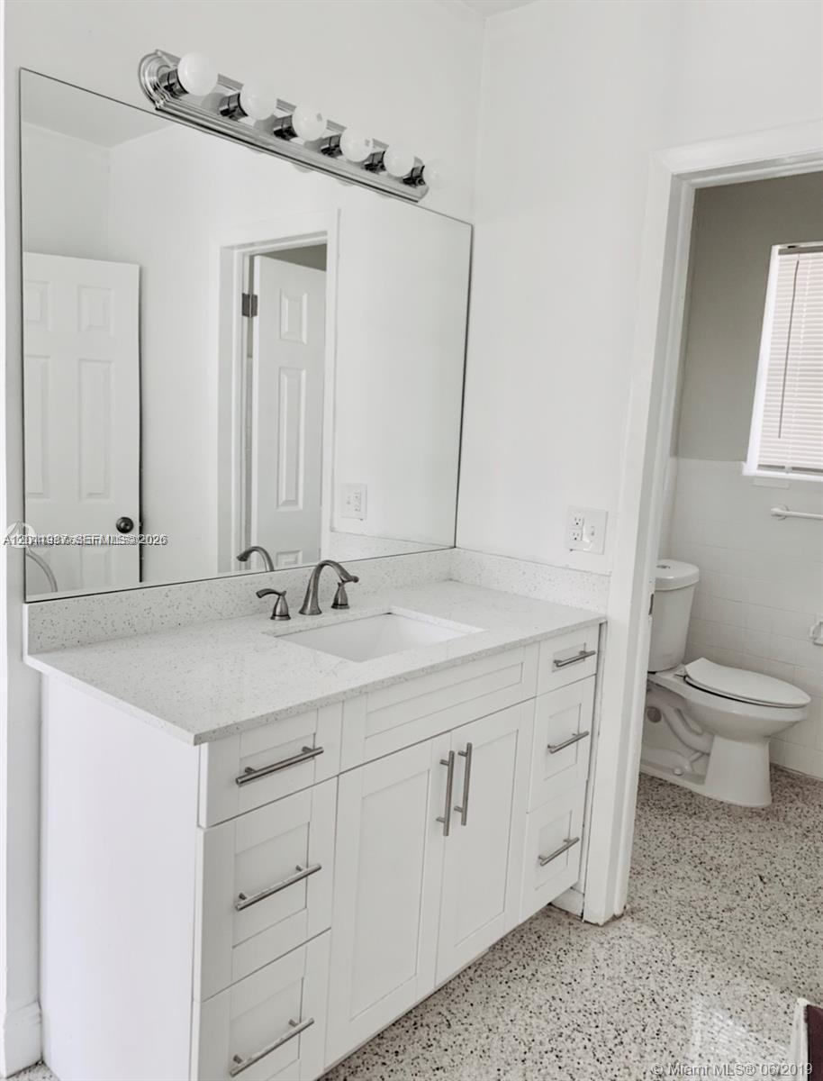 A bathroom features a white vanity with a speckled countertop, a large mirror, and a toilet — 7731 NW 2nd Ave # 6, Miami FL 33150, MIAMI, FL