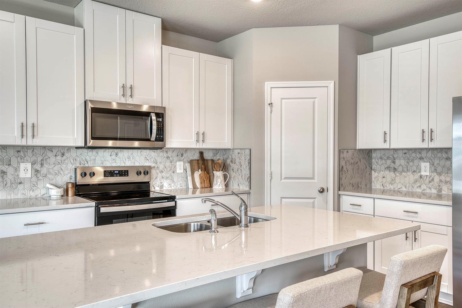 A kitchen features white cabinets, a quartz island with a sink, and marble-patterned tile backsplashes — 5735 SE Edgewater Circle, Stuart FL 34997, STUART, FL