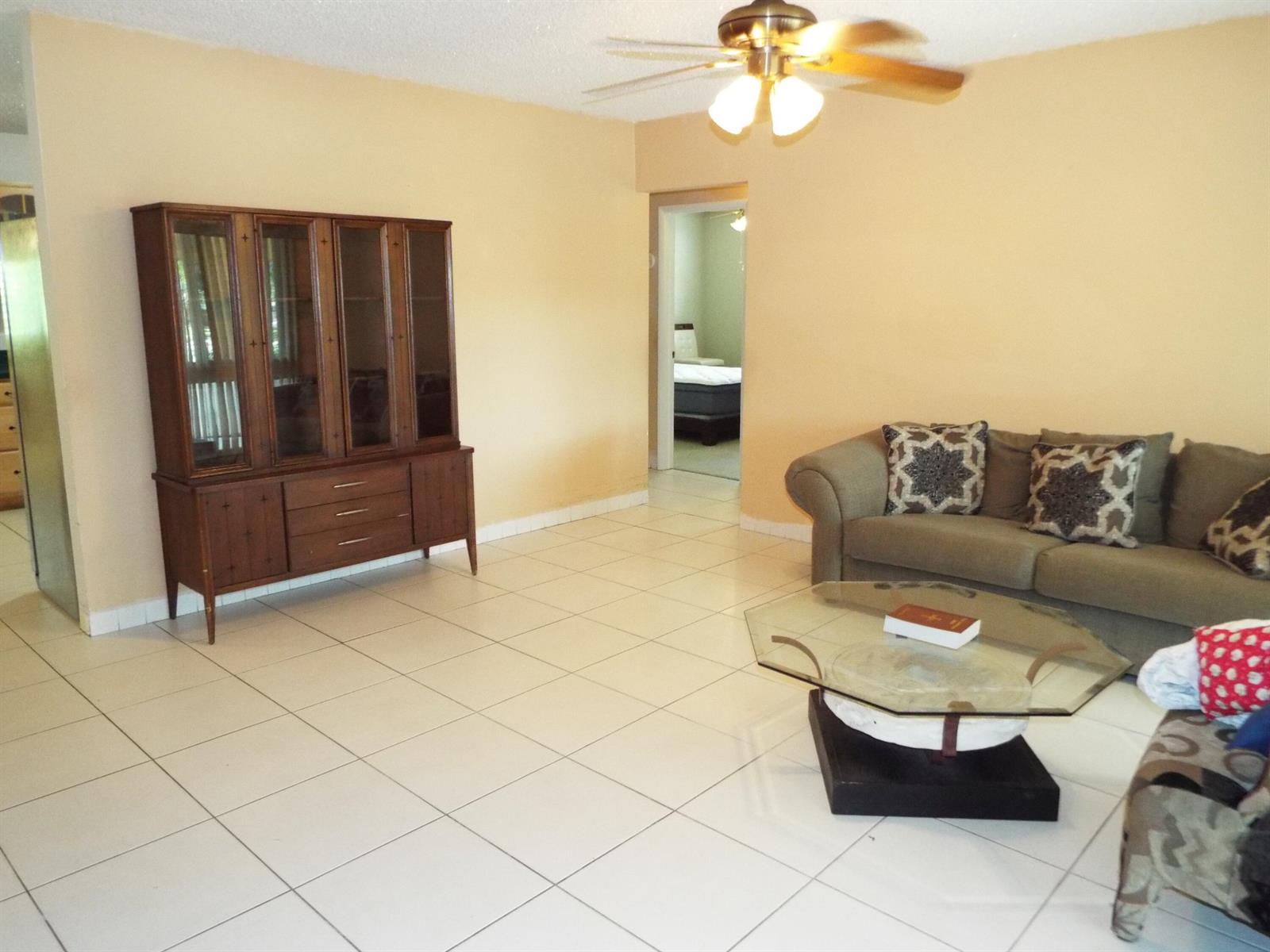 A living room with beige walls, white tile floors, a wooden hutch, and a sofa — 490 SE 3rd Avenue, Pompano Beach FL 33060, POMPANO BEACH, FL