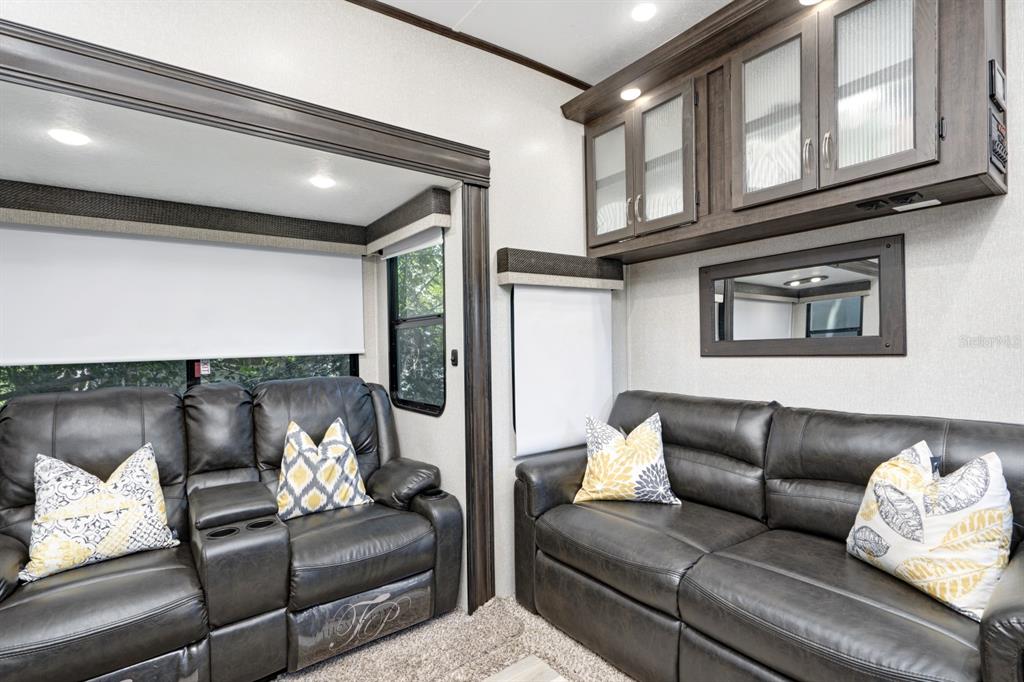 A living area features two dark leather sofas, overhead cabinets with glass doors, and windows — 305 LINDEN DRIVE UNIT Fifth wheel, ELLENTON, FL