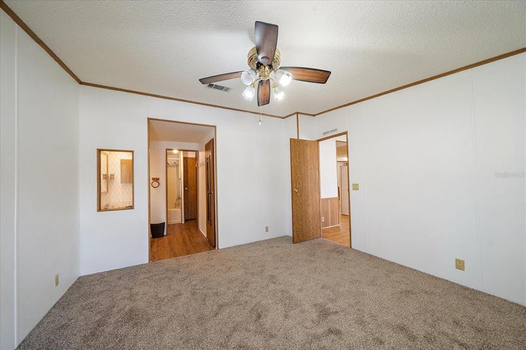 A bedroom with beige carpet, white walls, a ceiling fan, and two open doorways — 3028 BAMBOO COURT, PUNTA GORDA, FL