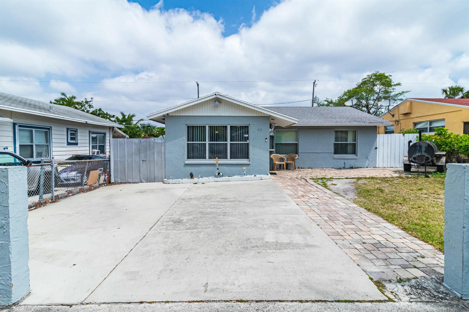 A single-story gray house features a concrete driveway, a brick walkway, and a fenced yard — 513 El Vedado, West Palm Beach FL 33405, WEST PALM BEACH, FL