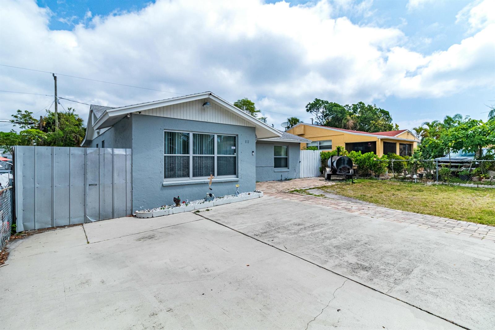 A gray single-story house features a concrete driveway, a metal fence, and a paved walkway — 513 El Vedado, West Palm Beach FL 33405, WEST PALM BEACH, FL
