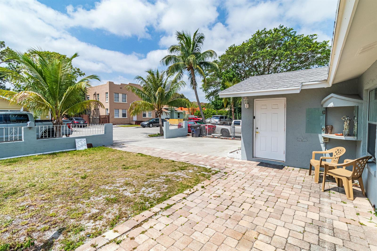 A paved patio area sits beside a gray house with a white door and palm trees — 513 El Vedado, West Palm Beach FL 33405, WEST PALM BEACH, FL