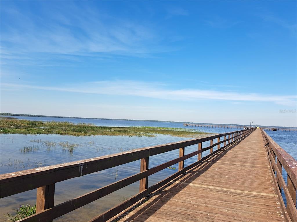 A long wooden pier extends over a lake with marshy vegetation under a blue sky — 20 AVOCADO DRIVE, INDIAN LAKE ESTATES, FL