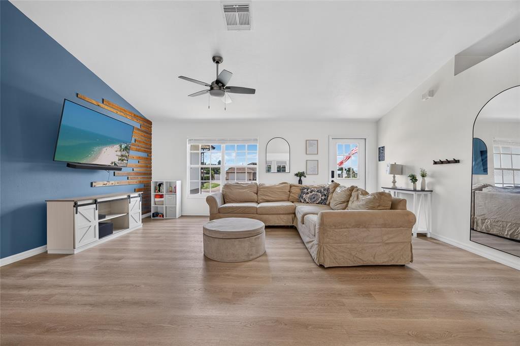 A living room features light wood flooring, a blue accent wall with wood slats, and a sectional — 1821 SW 22ND TERRACE, CAPE CORAL, FL