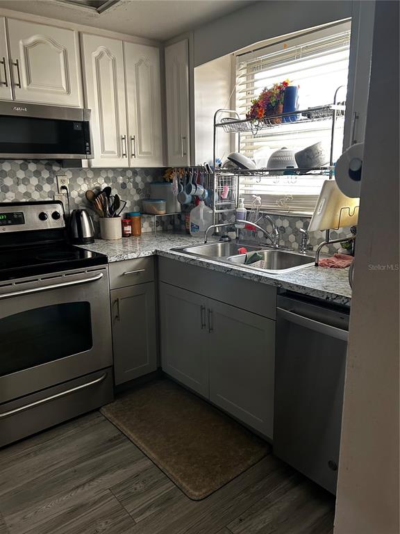 A kitchen features stainless steel appliances, white cabinetry, a double sink, and gray tile backsplash — 5059 LIVE OAK CIRCLE UNIT 5059, BRADENTON, FL