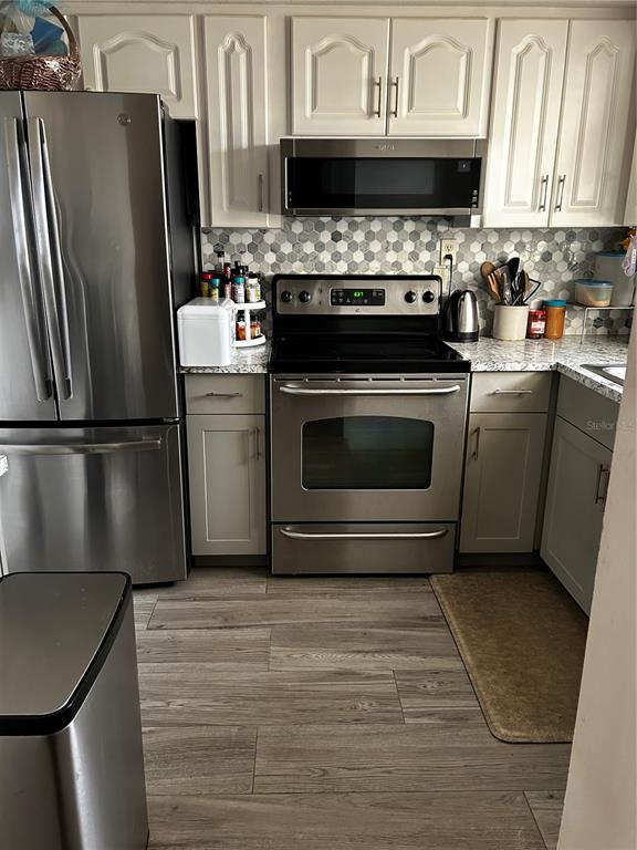 A kitchen features stainless steel appliances, white cabinetry, and a gray hexagonal tile backsplash — 5059 LIVE OAK CIRCLE UNIT 5059, BRADENTON, FL