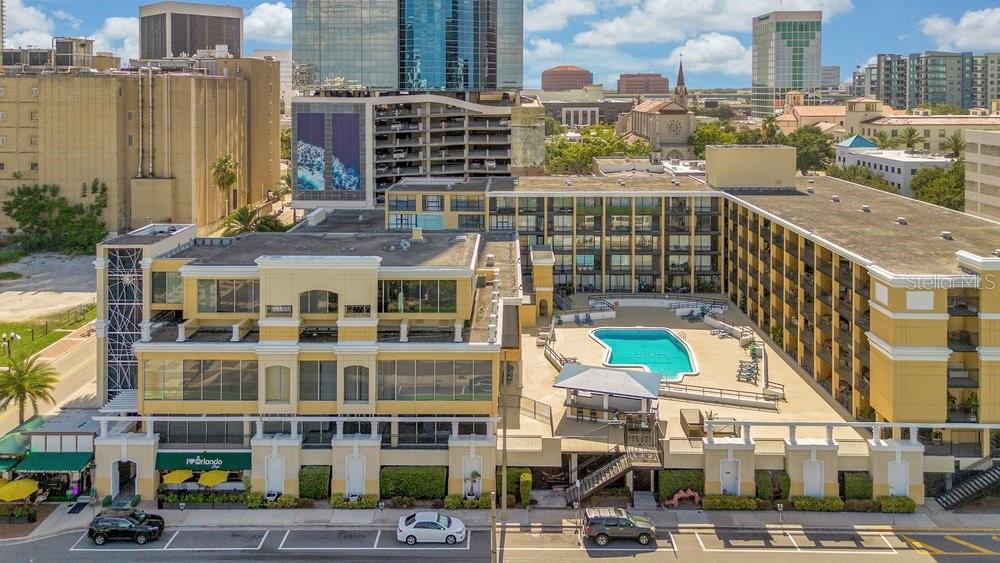 An aerial view of a yellow multi-story building featuring a swimming pool and parking area — 151 E WASHINGTON STREET UNIT 217, ORLANDO, FL