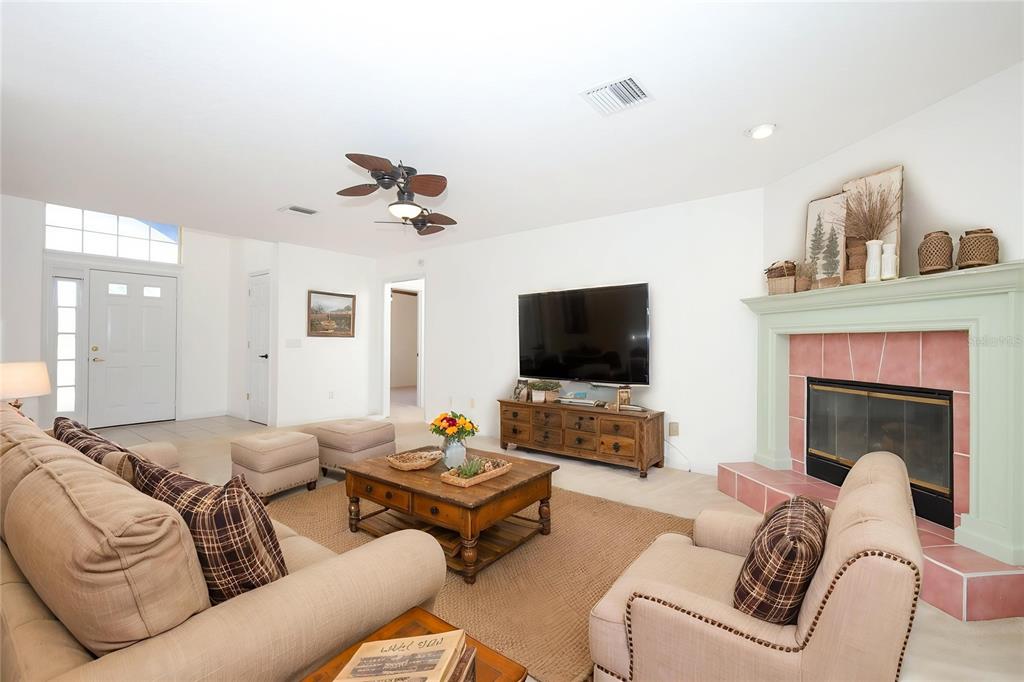 A living room features a fireplace with pink tiles, a television, and beige furniture — 1932 MONTEREY DRIVE, DELTONA, FL
