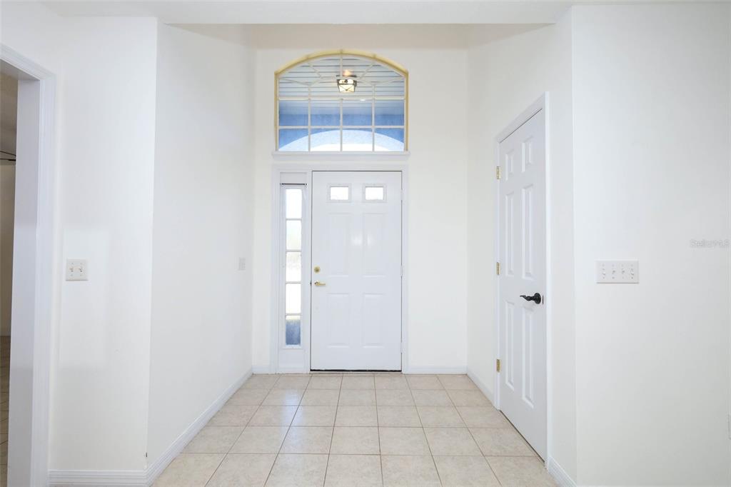 A bright entryway features white walls, tiled flooring, a front door, and an arched transom window — 1932 MONTEREY DRIVE, DELTONA, FL