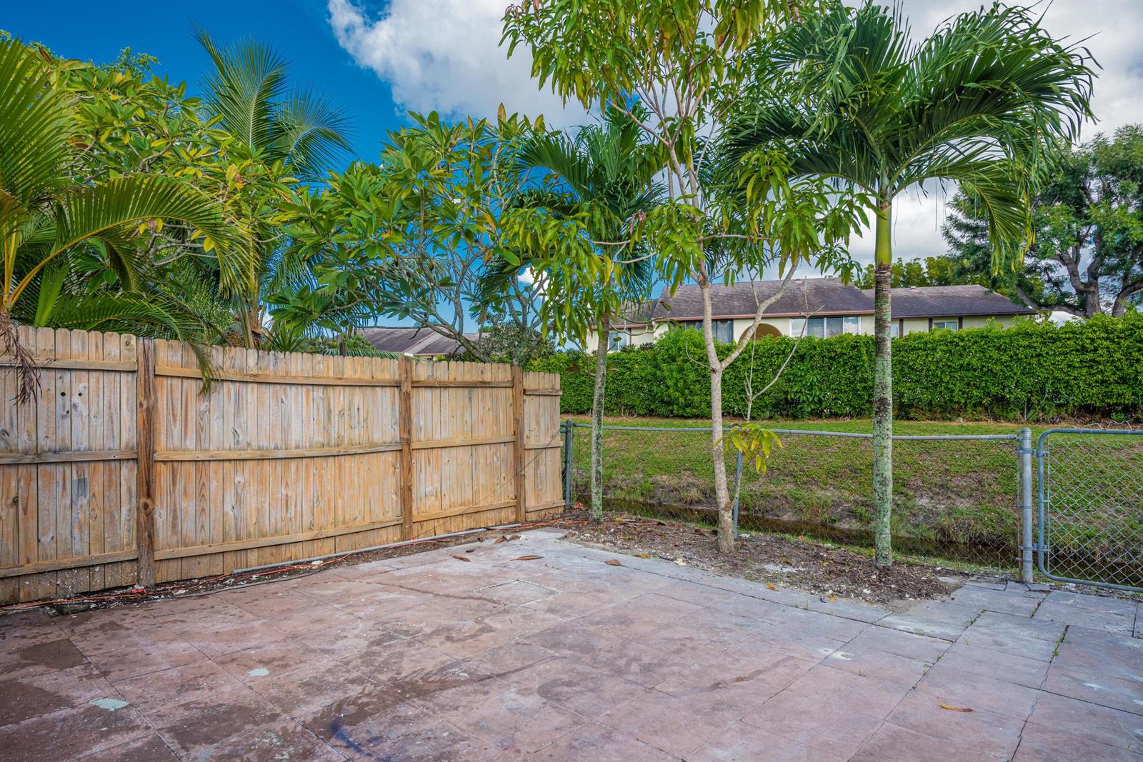 A paved patio area sits beside a wooden fence and palm trees in a backyard — 5847 S 37th Street, FL 33463, FL