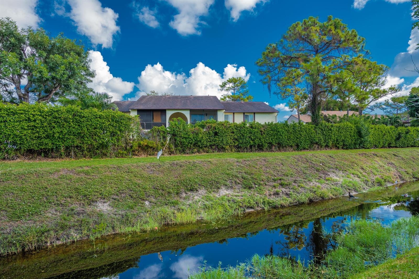 A two-story residential building sits behind a tall hedge and a grassy canal bank — 5847 S 37th Street, FL 33463, FL