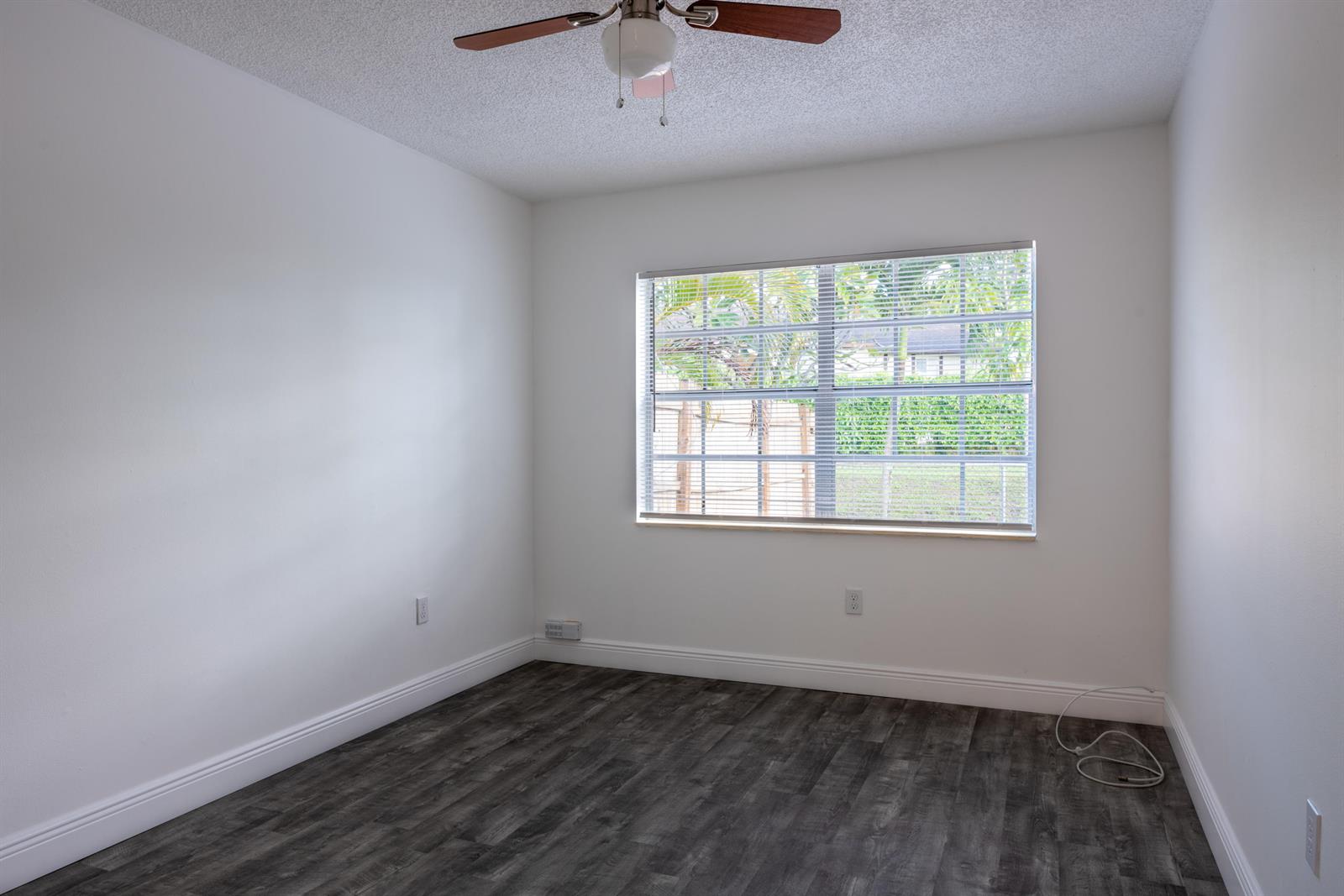An empty bedroom features white walls, dark wood-look flooring, a ceiling fan, and a window — 5847 S 37th Street, FL 33463, FL