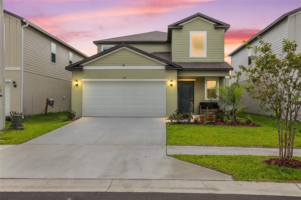 A two-story house with light green siding, a white garage door, and a concrete driveway — 629 BALD CYPRESS DRIVE, LAKELAND, FL