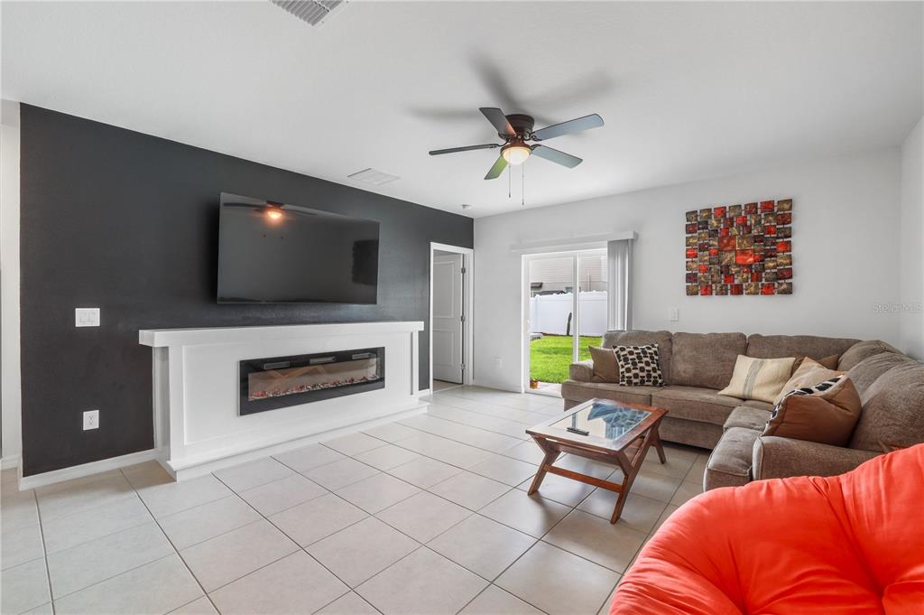 A living room features a dark accent wall with a fireplace, television, and tile flooring — 629 BALD CYPRESS DRIVE, LAKELAND, FL