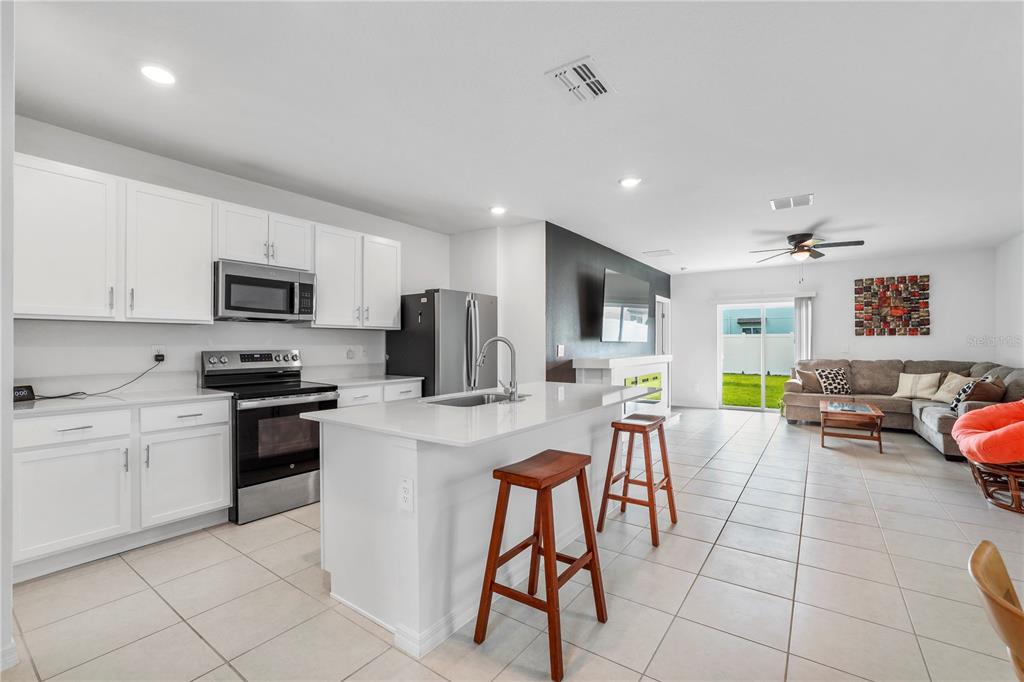 A kitchen with white cabinets and a center island opens into a living room area — 629 BALD CYPRESS DRIVE, LAKELAND, FL