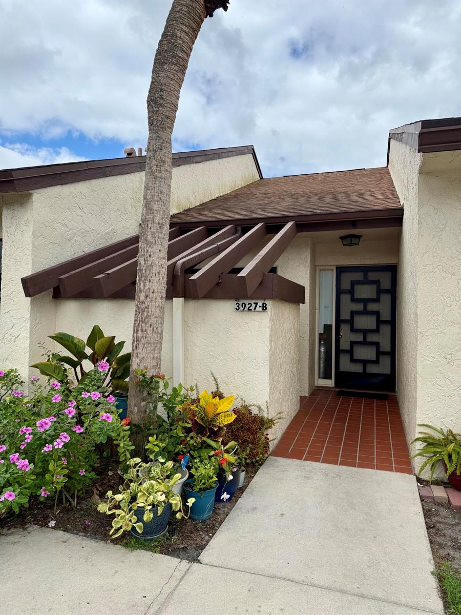 The exterior of a residential unit features a brown wooden pergola, a tiled entryway, and landscaping — 3927 Vine Tree Trail # B, Lake Worth FL 33467, LAKE WORTH, FL
