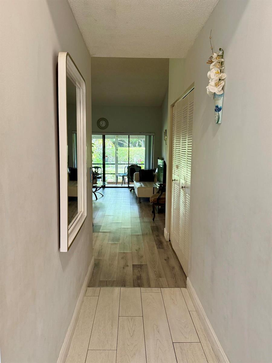 A hallway with light-colored tile flooring leads to a living area with wood-look floors — 3927 Vine Tree Trail # B, Lake Worth FL 33467, LAKE WORTH, FL