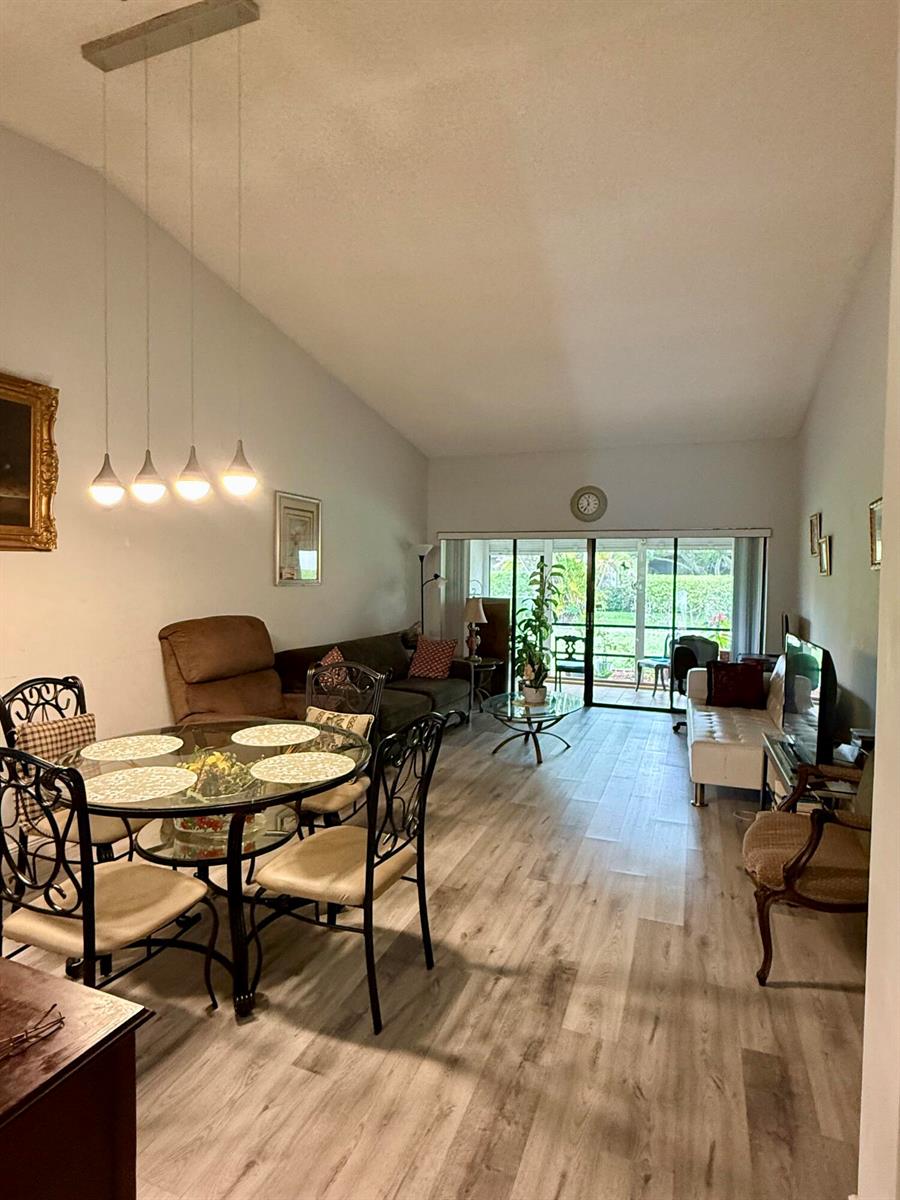A living and dining area with vaulted ceilings, wood-look flooring, and sliding glass patio doors — 3927 Vine Tree Trail # B, Lake Worth FL 33467, LAKE WORTH, FL