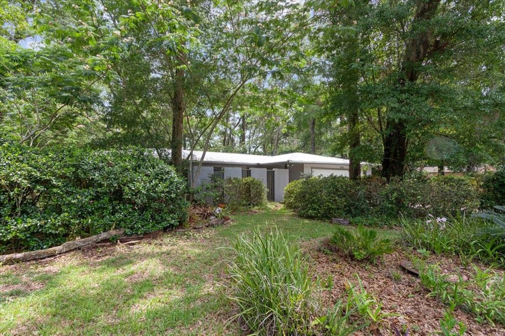 A single-story house with a white roof is partially obscured by trees and bushes — 4003 NW 34TH PLACE, GAINESVILLE, FL