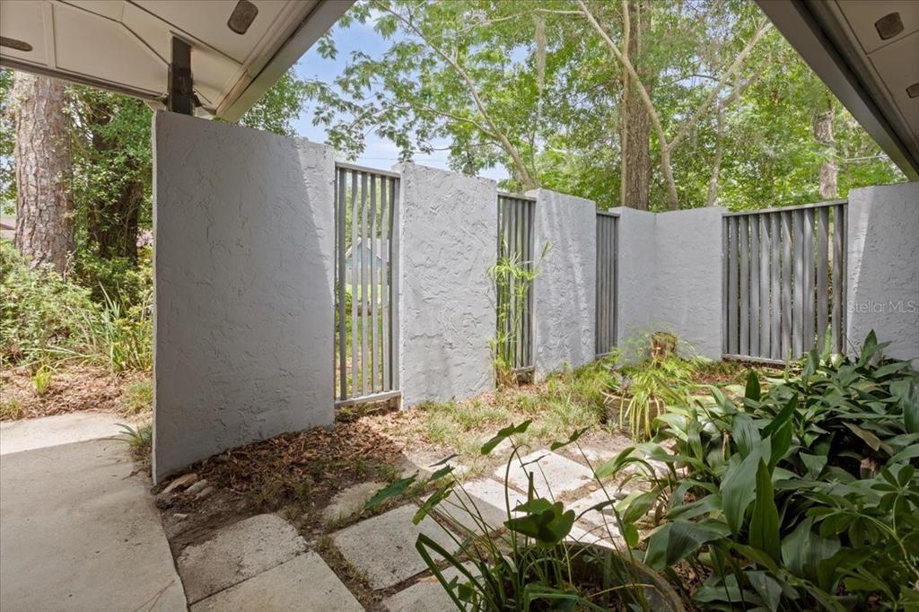 A covered patio features a textured gray privacy wall with vertical slat inserts and landscaping — 4003 NW 34TH PLACE, GAINESVILLE, FL