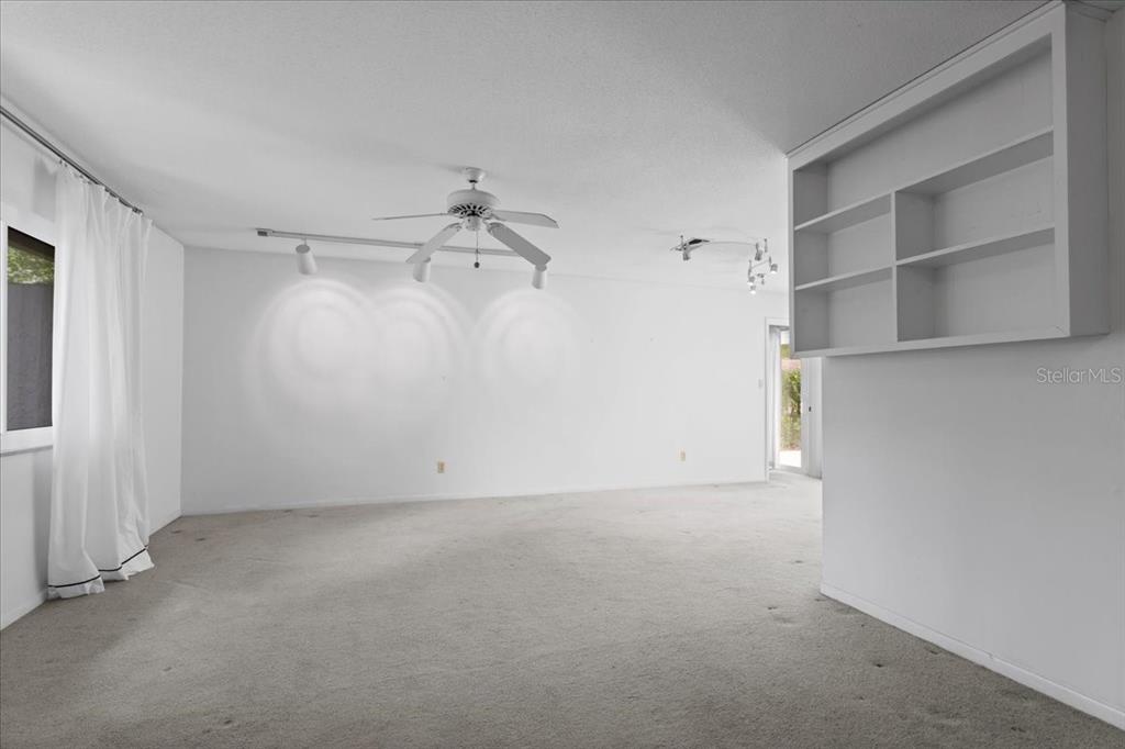 A spacious, white-walled room features beige carpeting, a ceiling fan, and built-in wall shelving — 4003 NW 34TH PLACE, GAINESVILLE, FL