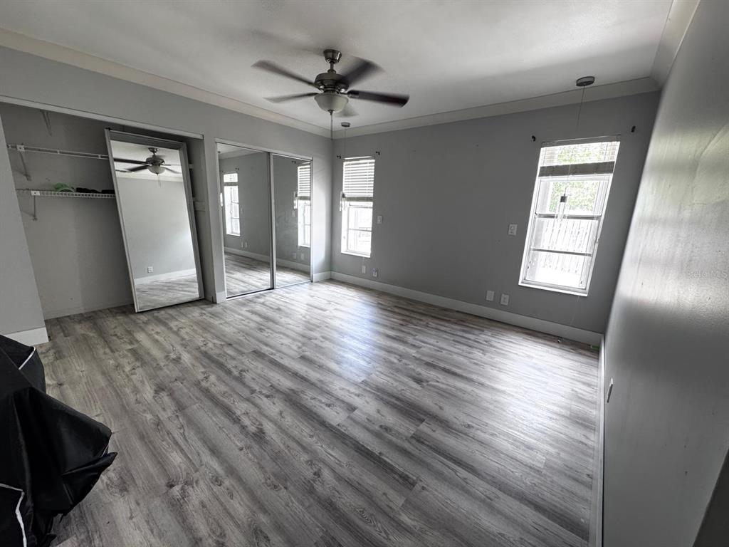 An empty bedroom features gray wood-look flooring, mirrored closet doors, and a ceiling fan — 11088 NW 23RD COURT, SUNRISE, FL