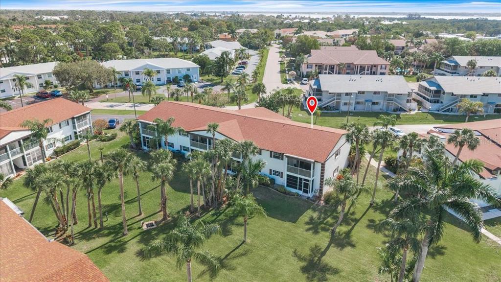 An aerial view shows a multi-story apartment building surrounded by palm trees and green lawns — 7043 NEW POST DRIVE UNIT 1, NORTH FORT MYERS, FL