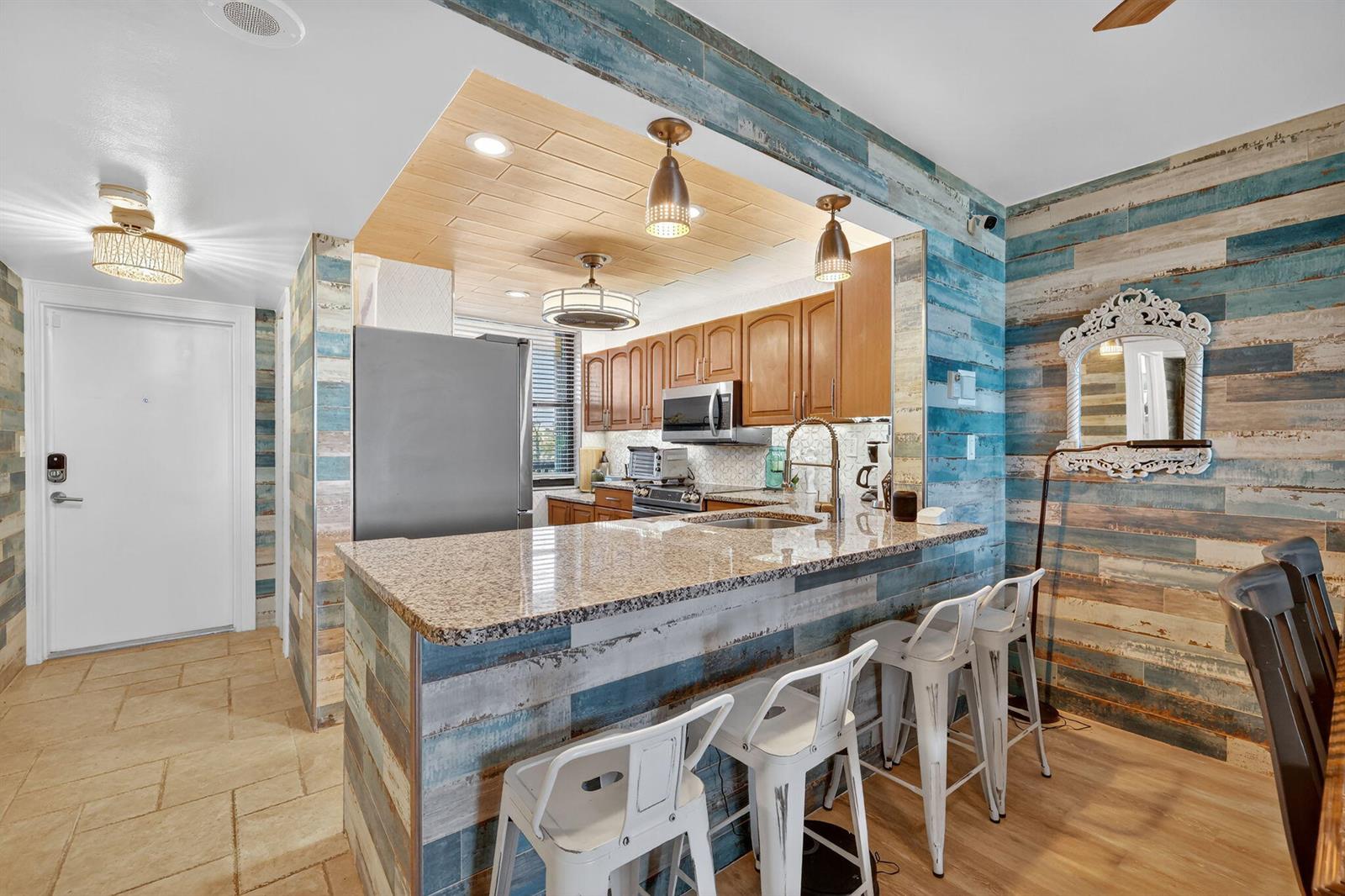 A kitchen with a granite breakfast bar, wooden plank walls, and white metal stools — 10680 S Ocean Drive # 105, Jensen Beach FL 34957, JENSEN BEACH, FL