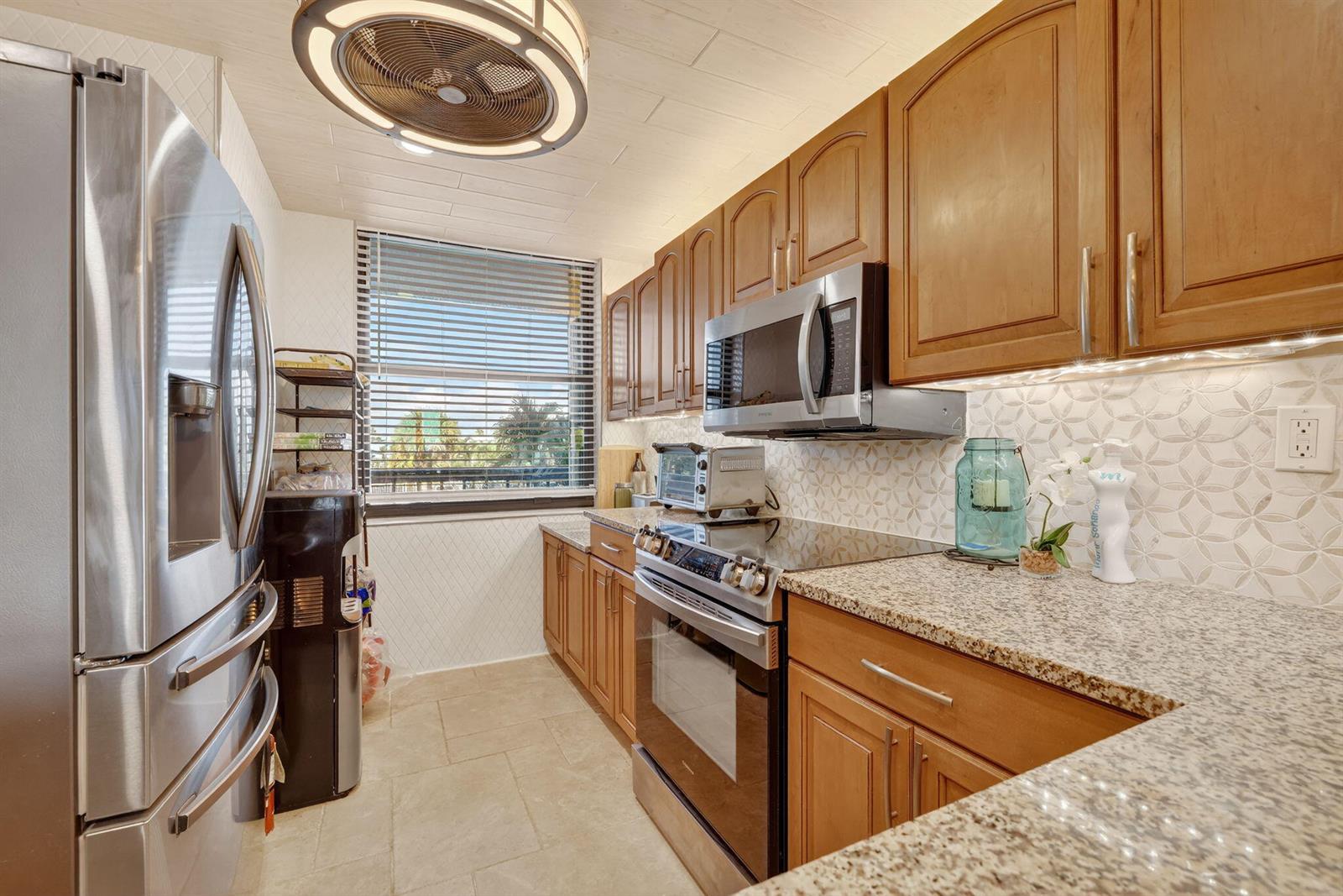 A galley kitchen features wood cabinets, granite countertops, stainless steel appliances, and a window — 10680 S Ocean Drive # 105, Jensen Beach FL 34957, JENSEN BEACH, FL