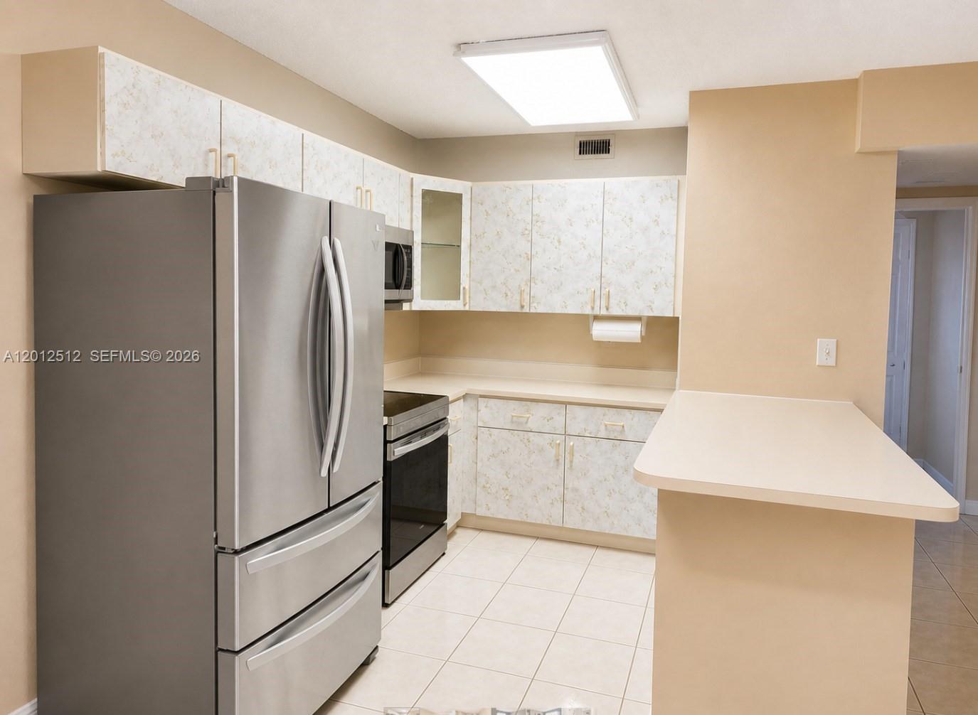 A kitchen features stainless steel appliances, patterned cabinets, and a beige breakfast bar — 15619 SW 73rd Cir Ter # 9, Miami FL 33193, MIAMI, FL