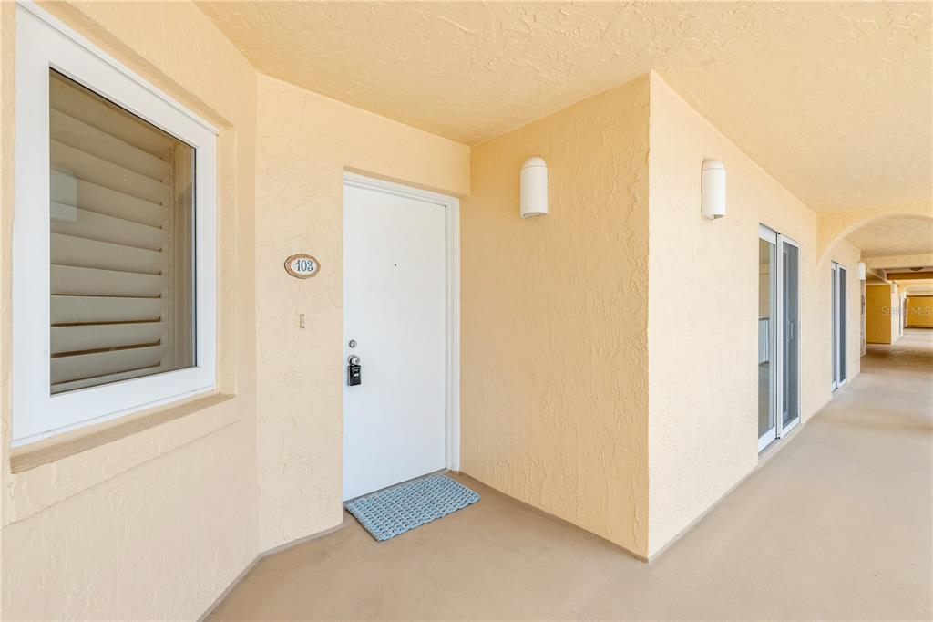 A white front door with a number 103 plaque sits on a beige exterior walkway — 257 MINORCA BEACH WAY UNIT 103, NEW SMYRNA BEACH, FL