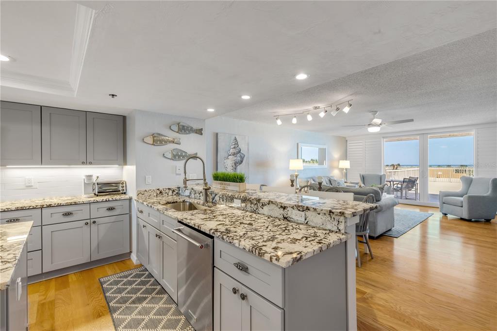 A kitchen with gray cabinets and granite countertops overlooks a living area with ocean views — 257 MINORCA BEACH WAY UNIT 103, NEW SMYRNA BEACH, FL