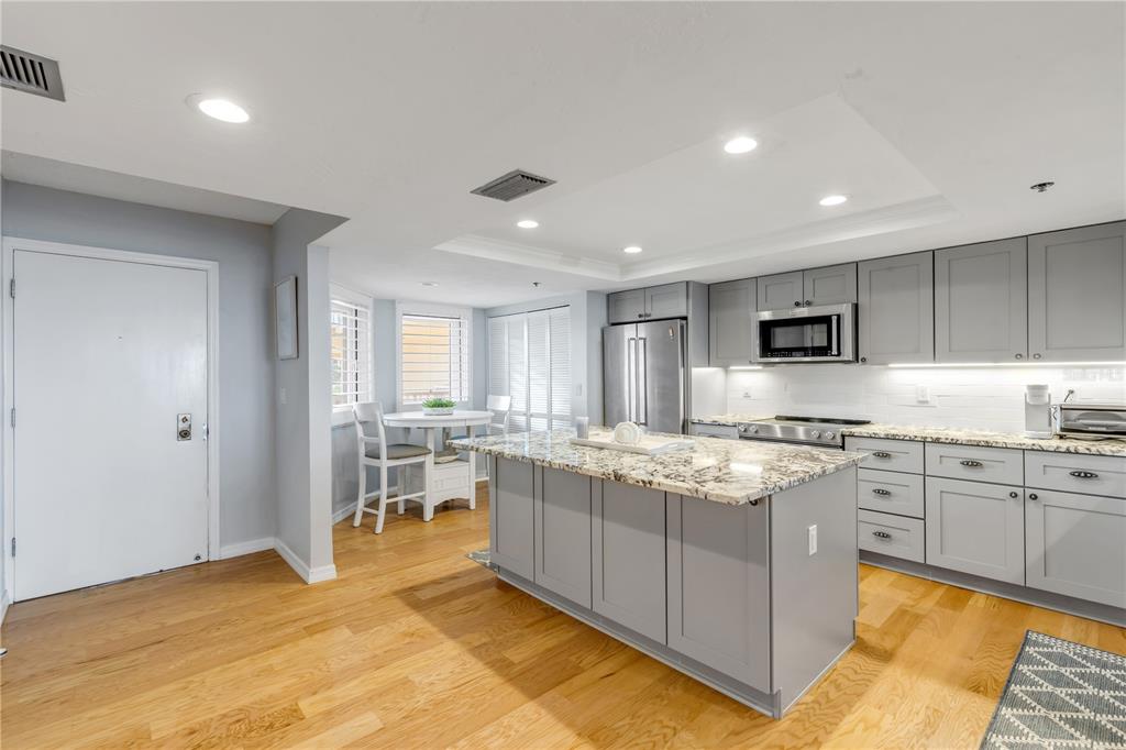 A kitchen with gray cabinets, granite countertops, a central island, and light wood flooring — 257 MINORCA BEACH WAY UNIT 103, NEW SMYRNA BEACH, FL