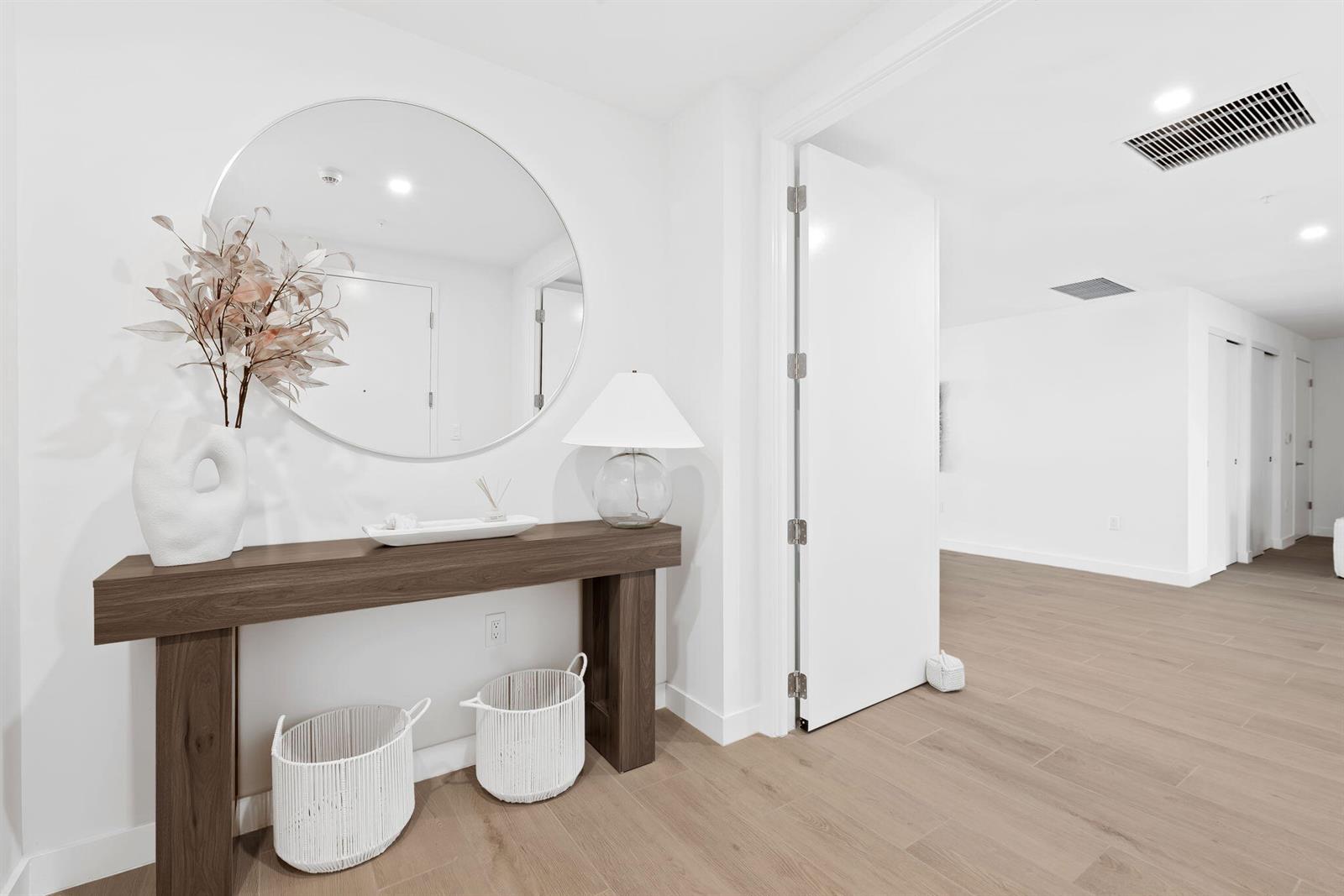 A modern entryway features a wooden console table, a round mirror, and white storage baskets — 900 N Ocean Boulevard # 1404, Pompano Beach FL 33062, POMPANO BEACH, FL